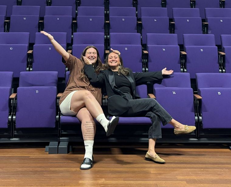 Shar en Floortje lachend op de paarse stoelen van een lege theaterzaal